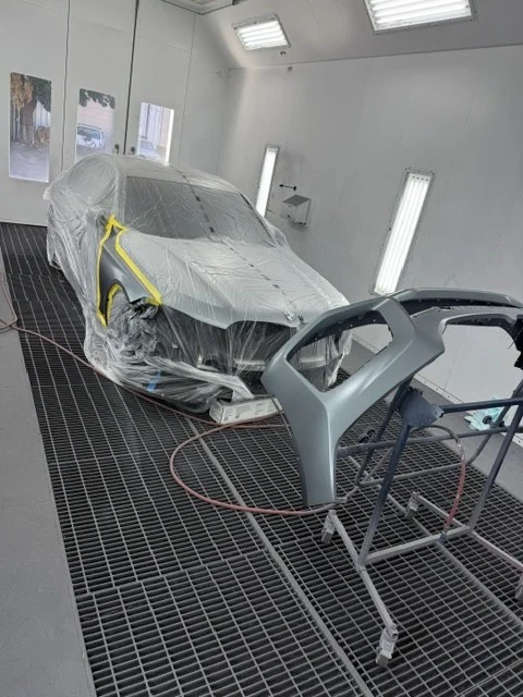 New OEM front bumper on a stand in the spray booth during refinishing
